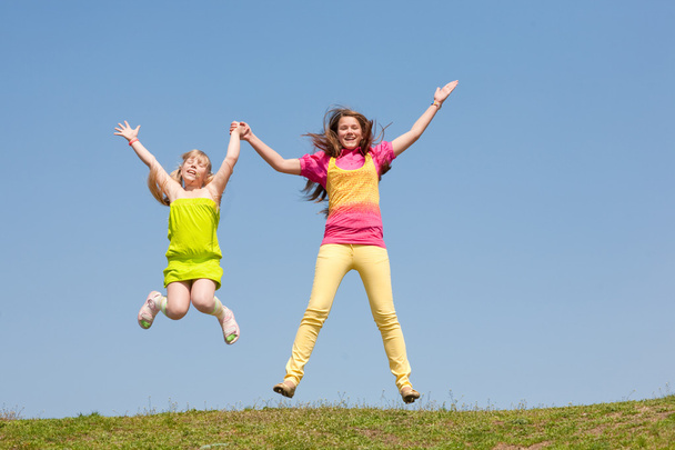 Two girls jumping on green meadow - Foto, Imagen