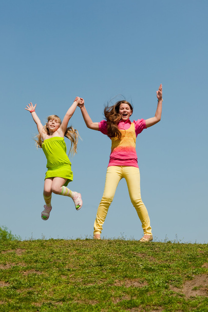 Two girls jumping on green meadow - Фото, зображення