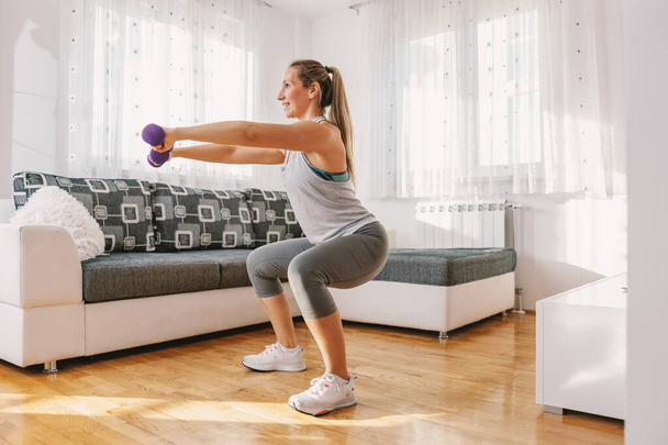Sorridente sportiva muscolare in forma facendo squat e tenendo i manubri. - Foto, immagini