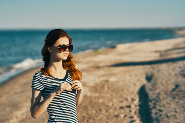 bela mulher em uma camiseta e óculos na praia perto do mar nas montanhas - Foto, Imagem