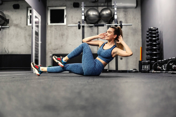 Eine Frau im Fitnessstudio macht Sit-Ups. Die fitte junge Frau macht ein Crunch-Workout, um ihren Bauch zu verbessern. Pumpen der Bauchmuskulatur und Stärkung des Körperkerns - Foto, Bild