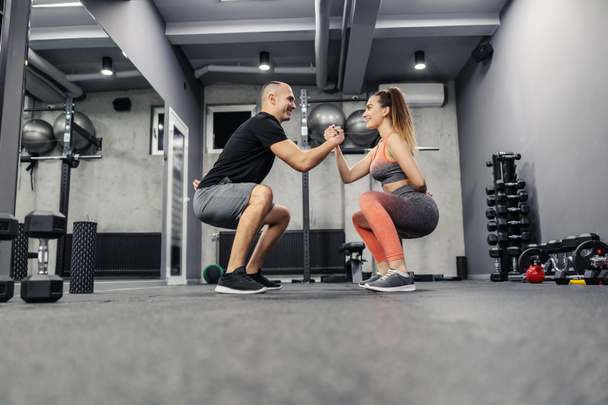 The concept of sports interesting and different fitness training. The couple does sports exercises together. They maintain balance by holding hands and doing squats, couple relationship goal - Photo, Image