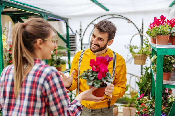Jardineiro sorridente vendendo flores para um cliente em pé em estufa. - Foto, Imagem