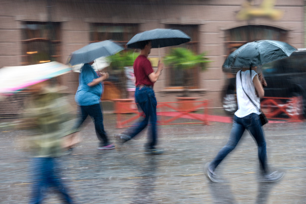 Grupa ludzi idąc ulicą na deszczowy dzień w ruchu - Zdjęcie, obraz