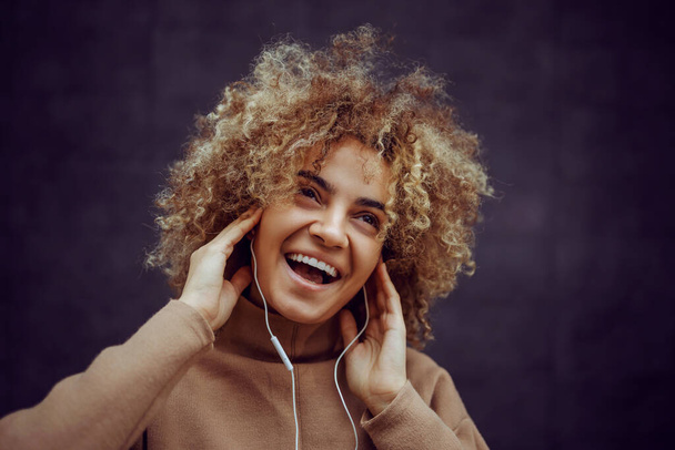 Meisje met een glimlach op haar gezicht hand in hand op haar oren en genieten van muziek. - Foto, afbeelding