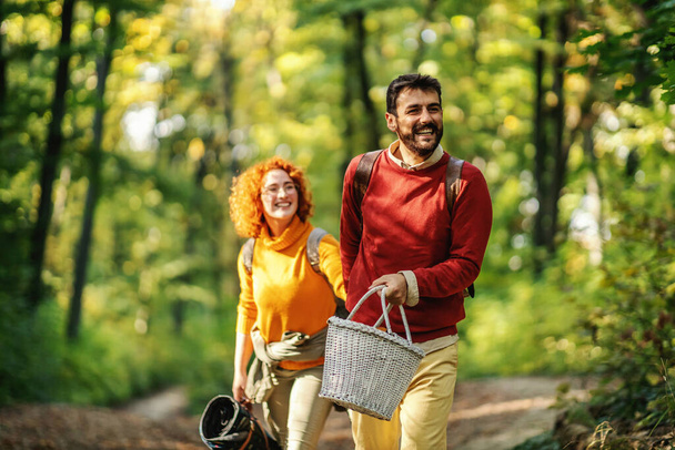 Young happy smiling couple in love holding hands and walking in nature. Couple is holding picnic equipment. Autumn time. - Photo, Image