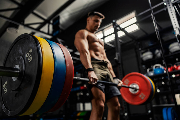 Weightlifting and the concept of sports life. A half-naked man stands in the middle of the gym and raises a barbell with weight plates. Dead lift with high load. Strength and energy, bodybuilding - Photo, Image