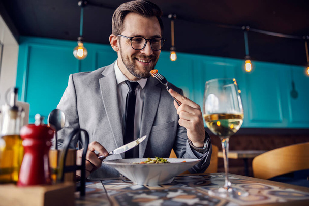 The man is about to take a bite of food, the man has lunch at a restaurant. A man elegantly dressed in a business suit eats and drinks in a restaurant. Business lifestyle, meals in restaurants - Photo, Image