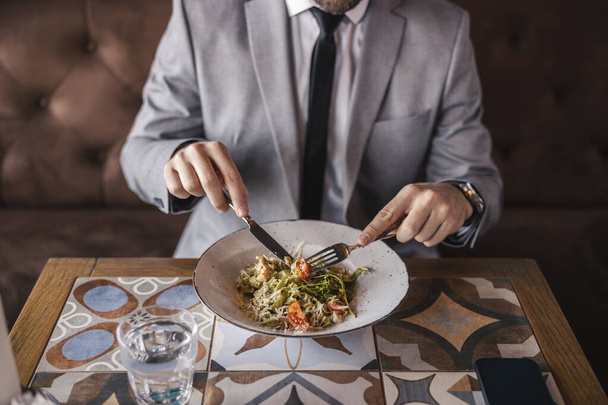 A delicious meal at the restaurant. A close-up shot of a plate with modern food eaten by a man in a business suit and with a watch around his wrist. Lunch meal, business lifestyle - Photo, Image