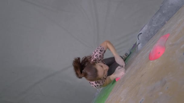 TOP DOWN: Νεαρή γυναίκα ορειβάτης κορυφές ένα βράχο σε μια εσωτερική εγκατάσταση κατάρτισης. - Πλάνα, βίντεο