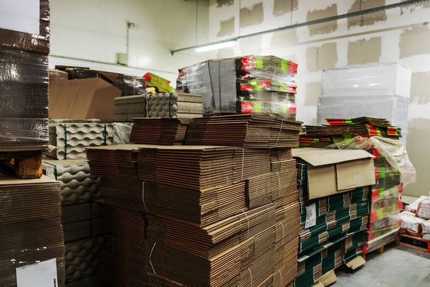Storage with stocks of unpacked cardboard boxes for packing goods. Large empty hall without people with a lot of cardboard. Stocks of raw materials for package distribution and logistics - Photo, Image