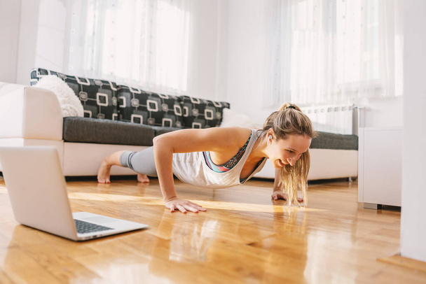 Mosolygó fitness oktató csinál deszkák a padlón otthon, és miután online osztály zárlat alatt. - Fotó, kép