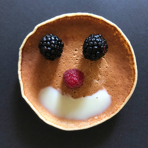 Smiley-Gesicht mit Pfannkuchen und Beeren auf schwarzem Hintergrund - Foto, Bild