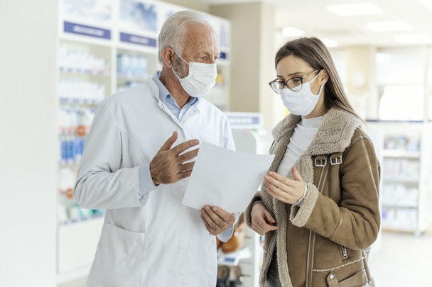 Reading prescription drugs, talking between a pharmacist and a client. An adult female customer seeks advice from an experienced pharmacist on the recommended therapy Protective masks and corona virus - Photo, Image