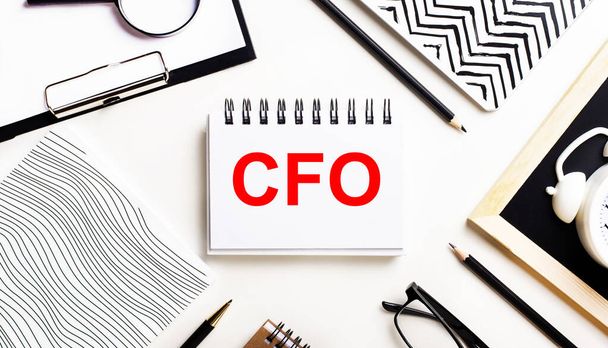 On a light table are notebooks, a magnifying glass, an alarm clock, glasses, and a pen. And in the center is a notebook with the text CFO Chief Financial Officer - Photo, image