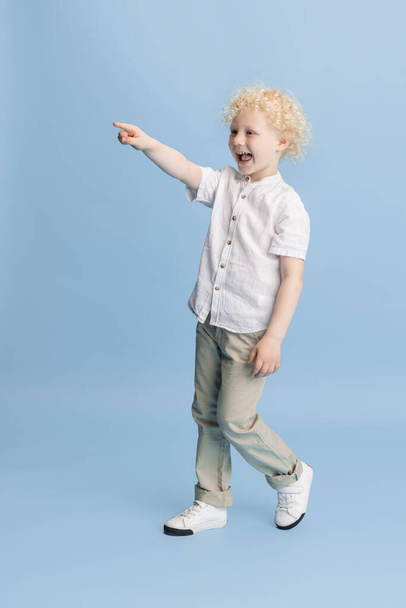Portrait of happy smiling boy posing isolated over blue studio background. - Foto, afbeelding