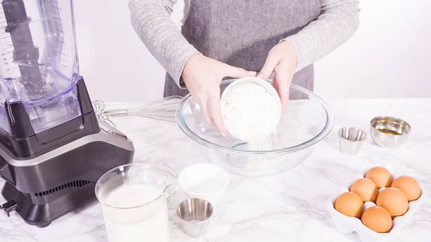 Mélange d'ingrédients dans un bol à mélanger en verre pour faire la pâte à crêpes. - Photo, image