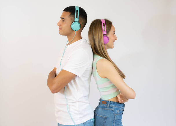 Happy loving couple. Studio shot of beautiful young couple listening music in casual clothes standing back to back and smiling - Photo, image