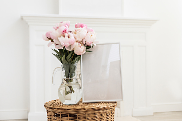 Vertical frame mockup on a wooden table in the kitchen. Glass vase with a bouquet of pink peonies. Scandinavian style interior. - Photo, Image
