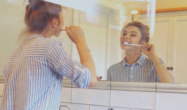 Young pretty woman brushing teeth in front of the mirror - Foto, Bild