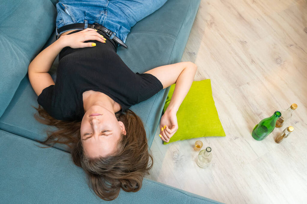 Betrunkene junge dunkelhaarige Frau schläft auf der Couch nach einer Party oder Stress mit leeren Flaschen auf dem Boden, Draufsicht aus dem Kopierraum - Foto, Bild