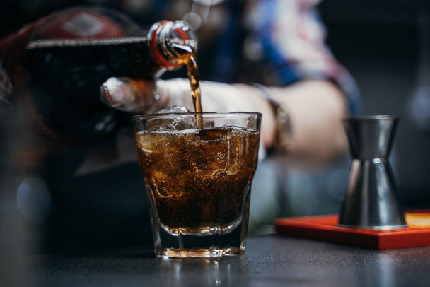 the bartender pours the client into an alcoholic drink whiskey cola with ice, a strong drink - Photo, Image