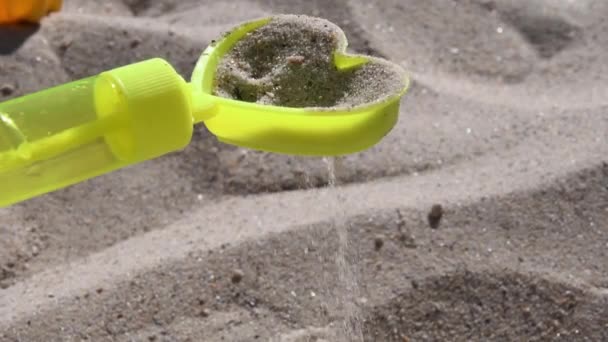 Jouet jaune sable tamiseur en forme de coeur avec coulée de grains de sable sur la plage - Séquence, vidéo