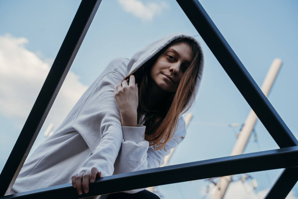 A girl in a white sweatshirt stands on the steel frame of the building - Фото, изображение