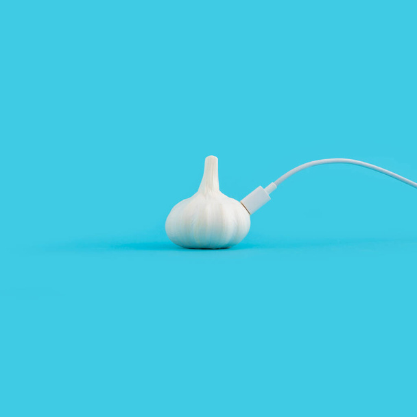 A white phone charger attached to a garlic isolated on a blue background - Foto, immagini