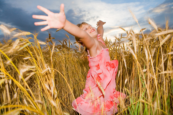 Little girl jumps in a wheat field. Against backdrop of cloudy s - 写真・画像