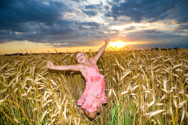 La niña salta en un campo de trigo. Contra el telón de fondo de cielos nublados
 - Foto, imagen