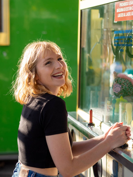 A young blonde female smiling at the cashbox at an amusement park - Zdjęcie, obraz