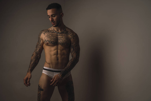 A young handsome muscular Caucasian male with tattoos wearing underwear and posing in a studio - Foto, imagen