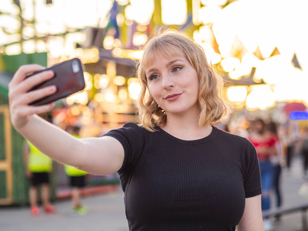 A young blonde female taking a selfie at an amusement park - 写真・画像
