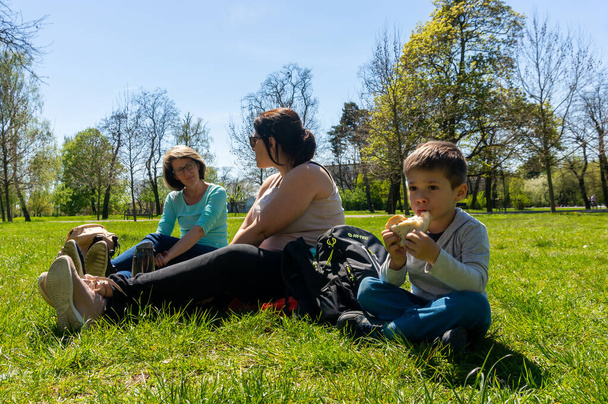 POZNAN, POLAND - May 09, 2021: Two women and a boy sitting on green grass at a park on a sunny spring day. - Фото, изображение