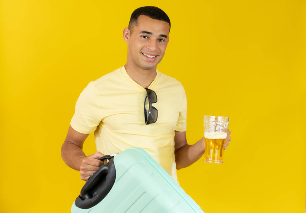 Молодой красивый мужчина держит чемодан и пьет пиво. Концепция праздника. - Фото, изображение