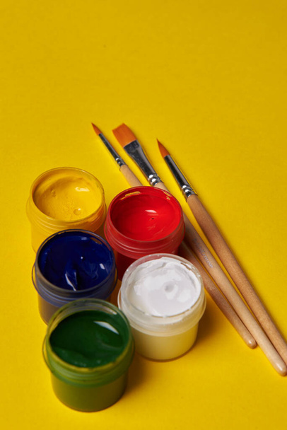 Sarı arka planda fırçalar ve renkli boya kutuları - Fotoğraf, Görsel