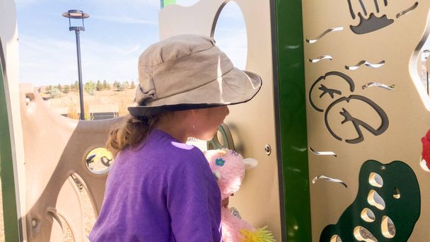 Mała dziewczynka bawiąca się na nowoczesnym placu zabaw dla dzieci na przedmieściach w upalny letni dzień. - Zdjęcie, obraz