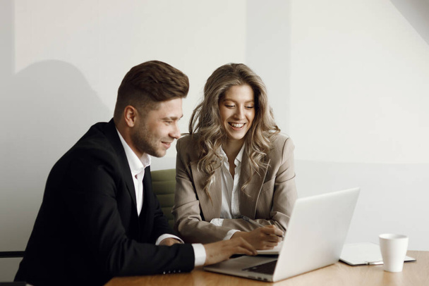 A man and a woman discuss business matters. A couple working at a laptop and blueprints in their home office smile. - Valokuva, kuva