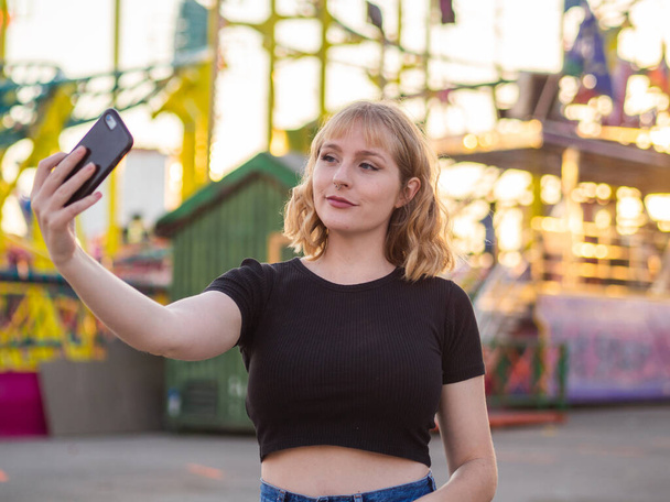 A Spanish blonde woman doing a selfie in an amusement park - Photo, image