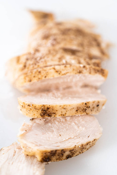 Trancher la poitrine de poulet fraîchement cuite sur une planche à découper blanche. - Photo, image