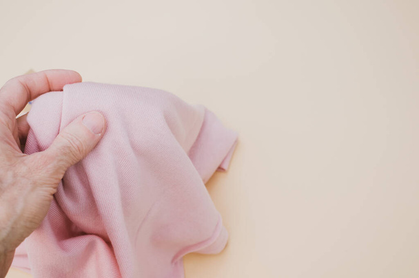 A hand grabbing a pink piece of fabric on a pastel background with copy space - Foto, Imagem