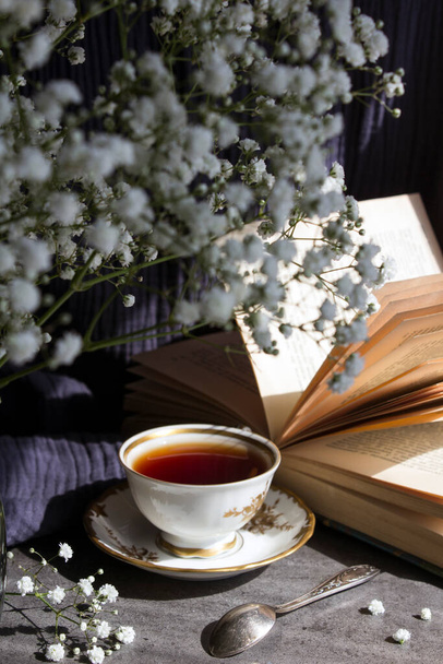 Stilleven met een kop thee. Eenvoudige compositiefoto met kleine witte bloemen en een kopje zwarte thee op een tafel. Prachtige ochtendfoto.  - Foto, afbeelding