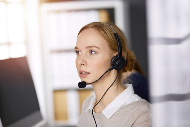 Businesswoman talking by headset while sitting in sunny office. Call center and diverse people group in business - Foto, Bild