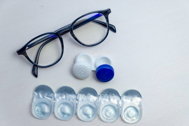 Contact lenses, contact lens packaging and lens container, on white surface. Vision correction and the alternative between glasses and contact lenses.  - Photo, Image