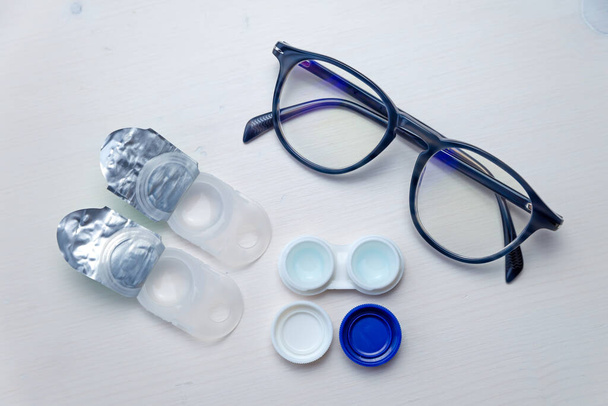Kontaktlencsék, kontaktlencse csomagolás és lencse tartály, fehér felületen. Látásjavítás és alternatíva a szemüveg és a kontaktlencse között.  - Fotó, kép
