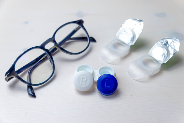 Lentes de contacto, embalaje de lentes de contacto y contenedor de lentes, en superficie blanca. Corrección de la visión y la alternativa entre gafas y lentes de contacto.  - Foto, Imagen
