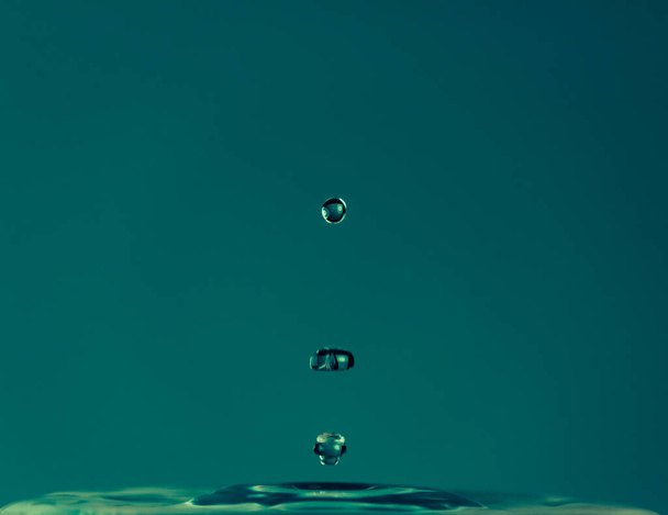 Kropelka wody spada i chlapie na niebieskie tło. Makro zdjęcie natury - Zdjęcie, obraz