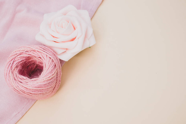 A delicate rose next to a pink ball of yarn on a pastel background with copy space - Zdjęcie, obraz