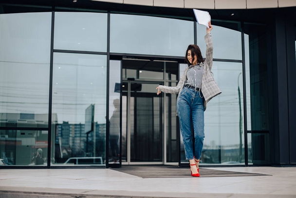 Small business owner office worker woman standing outside building with documents, smiling. Female mexican latin american successful executive girl wait colleague meeting. Copy space. - Zdjęcie, obraz